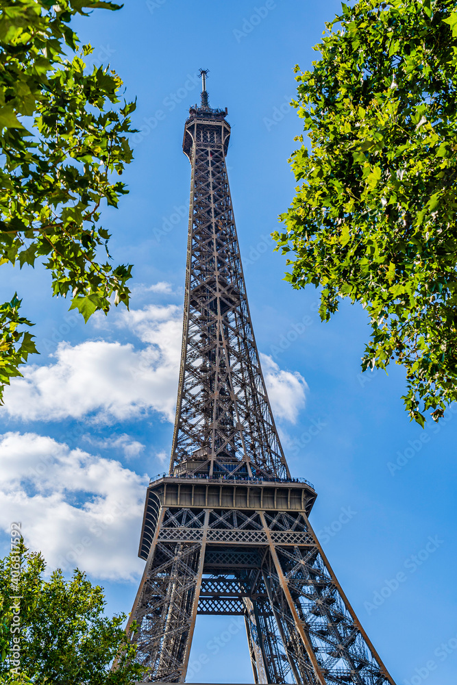 The Eiffel Tower surrounded by green tree leaves in Paris, France on a blue sky with white clouds background
