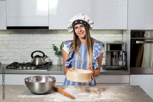 Close-up woman in kitchen sifting flour.