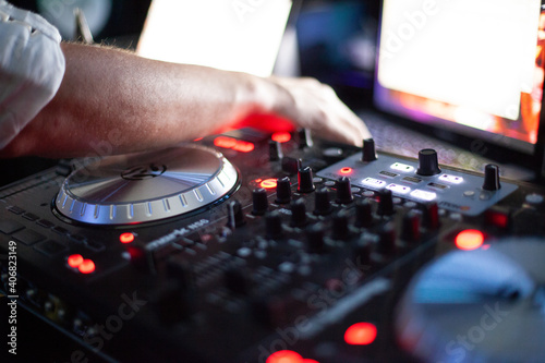 A DJ's hand reaches across his mixing table. 
