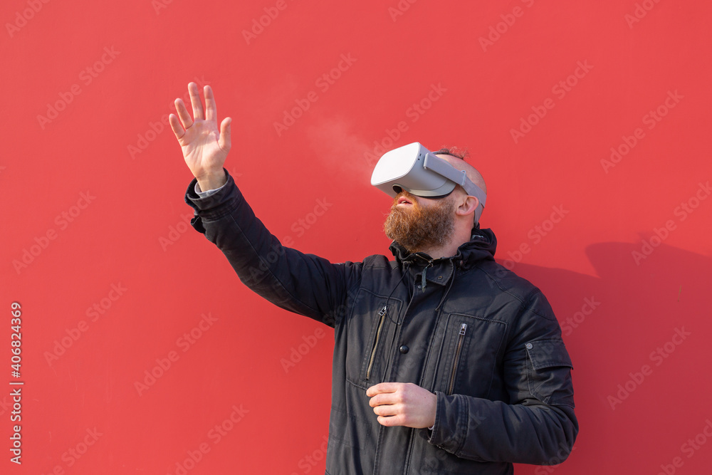 Emotional portrait of a man on the street wearing reality glasses against the background of a red wall Emotional portrait of a man on the street wearing reality glasses against the background of a red wall