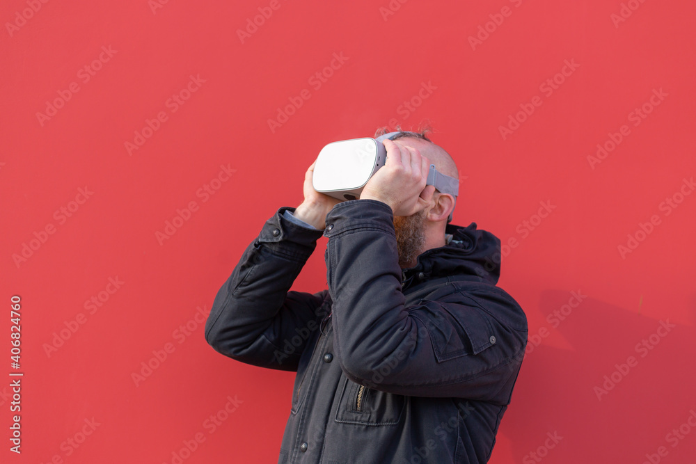 Emotional portrait of a man on the street wearing reality glasses against the background of a red wall Emotional portrait of a man on the street wearing reality glasses against the background of a red wall