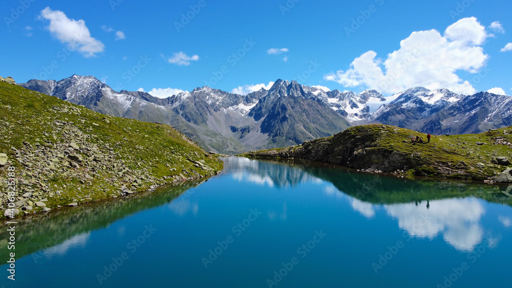 Fototapeta premium Perler See Bergsee in den Alpen, Berge mit See und blaues Wasser in Felsen mit Grün und Schnee beim Wandern für eine Auszeit und Erholung bei blauem Himmel