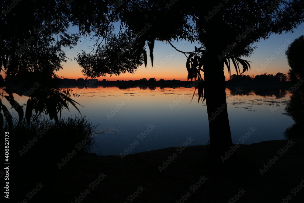 Sunset on the lake. Lake surrounded by trees at sunset. Sunset beach by the lake.