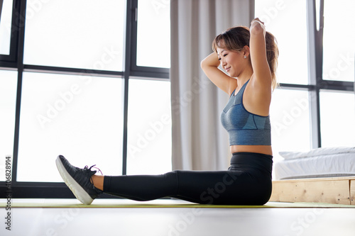 asian woman pulls her hair into a ponytail before exercising, sitting on mat, enjoying healthy lifestyle