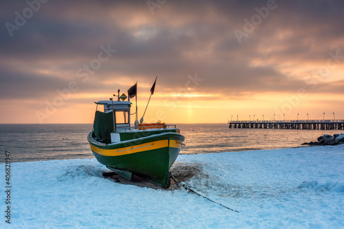 Fishing boat on snowy beach in Gdynia Orlowo at sunrise, Baltic Sea. Poland