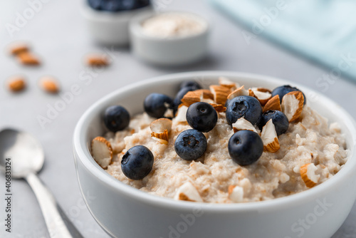 Oatmeal porridge in a bowl with blueberries and almonds on grey stone background. Concept of healthy breakfast, food, and lifestyle