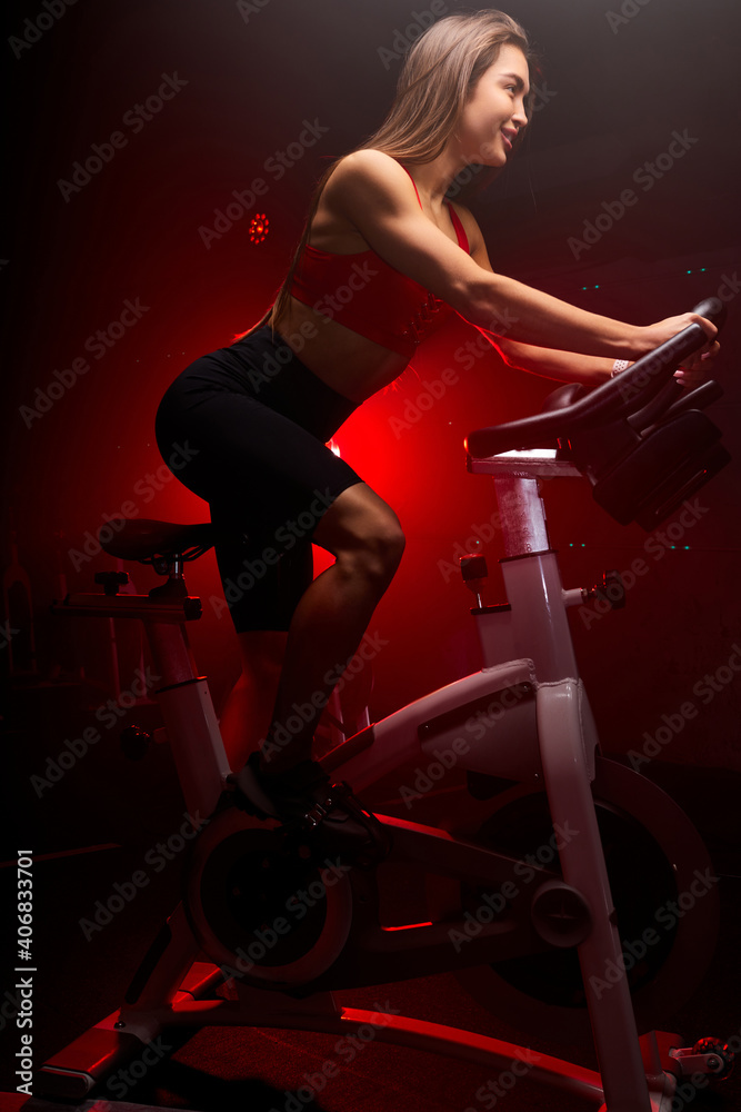 sude view on fitness woman cyclist, sits on bicycle and smile, enjoy workout training. she is exercising at gym, cycling on the trainer sude view on fitness woman cyclist, sits on bicycle and smile, enjoy workout training. she is exercising at gym, cycling on the trainer