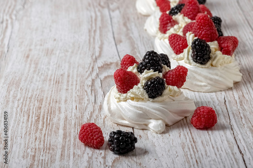 Homemade delicious Pavlova meringue cake with fresh raspberries and blackberries on a wooden background. Close-up. Copy space.