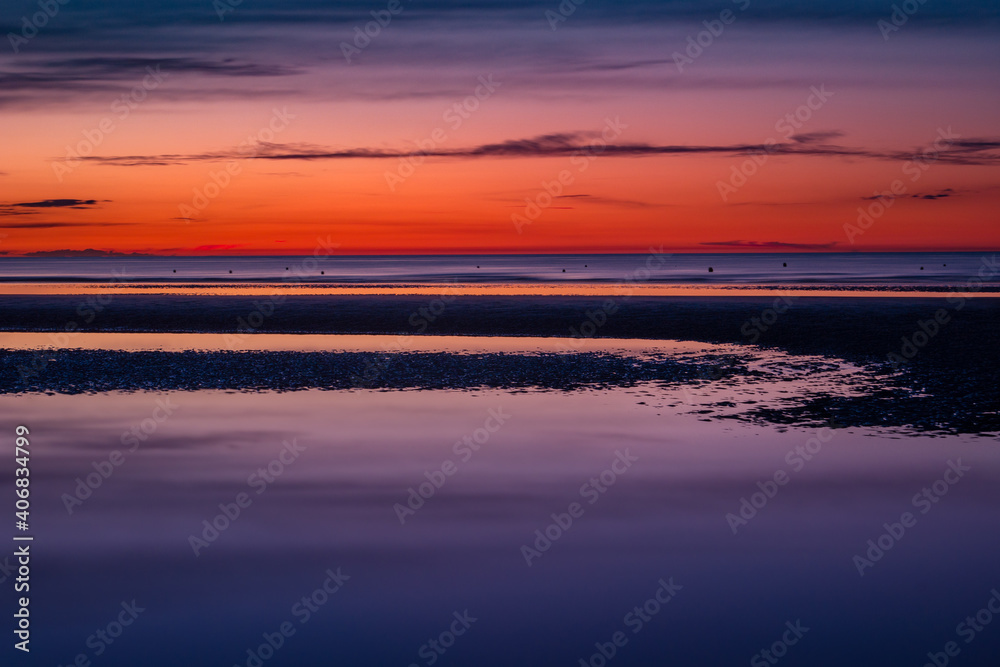 Obraz premium Purple and orange scenery at the beach just after sunset at low tide