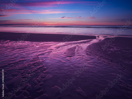 Colorful purple sunset at the beach with sand ripples in the foreground at low tide