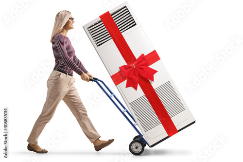 Woman pushing a hand-truck with a self standing ac unit tied with red ribbon