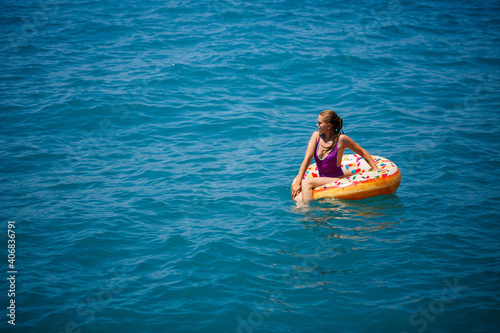 Young woman floating on an inflatable big donut in the transparent turquoise sea. View of a slender lady relaxing on vacation in Turkey, Egypt, Mediterranean Sea.