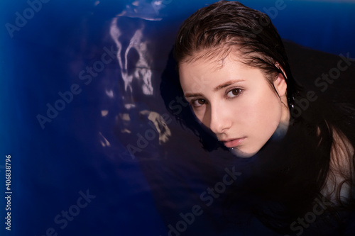 portrait of attractive brunette woman topless in blue liquid. in bathtub with colored water. drowning girl