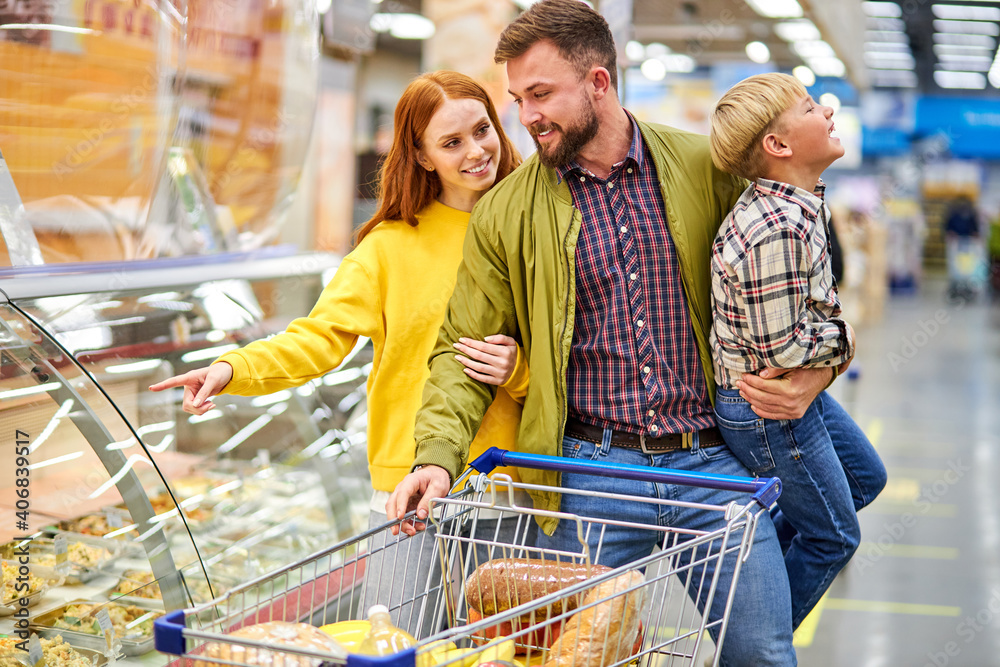 parents with restless son in grocery store, woman choosing food for dinner while her husband holds son in hands, near showcases with food