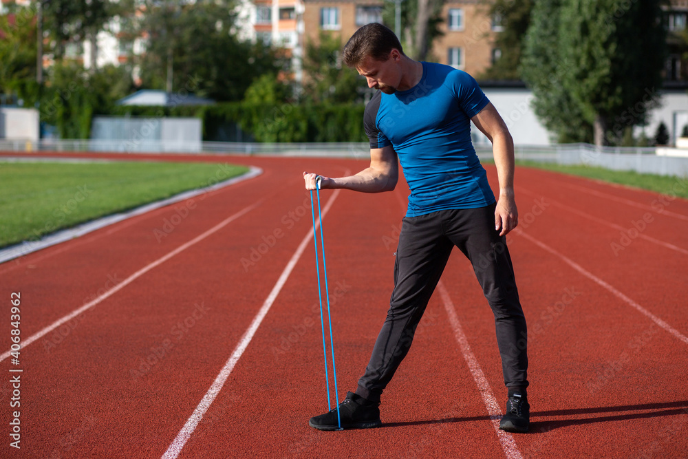 Sporty guy having workout with rubber band outside