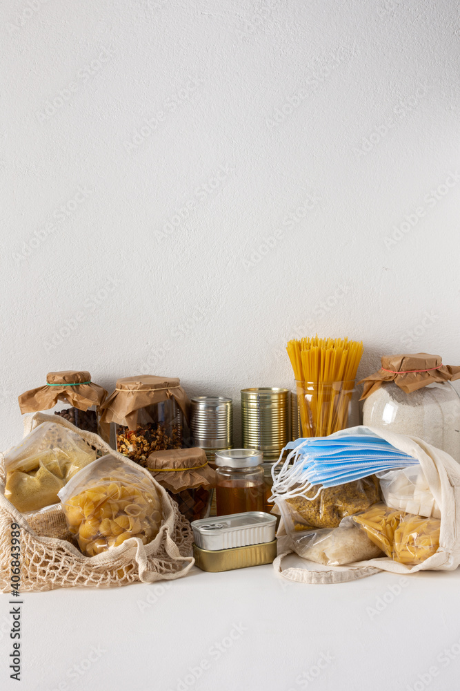 Naklejka premium Necessary food for the period of quarantine and isolation, the concept of staying at home, canned food and bags of cereals, various pasta and flour, honey and coffee, protective masks