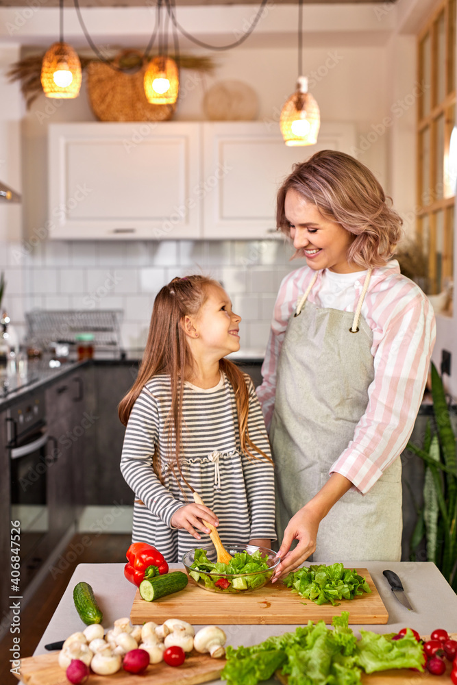 family mother with daughter cooking together, happy girl is glad to help mother preparing salad, mixing fresh vegetables family mother with daughter cooking together, happy girl is glad to help mother preparing salad, mixing fresh vegetables