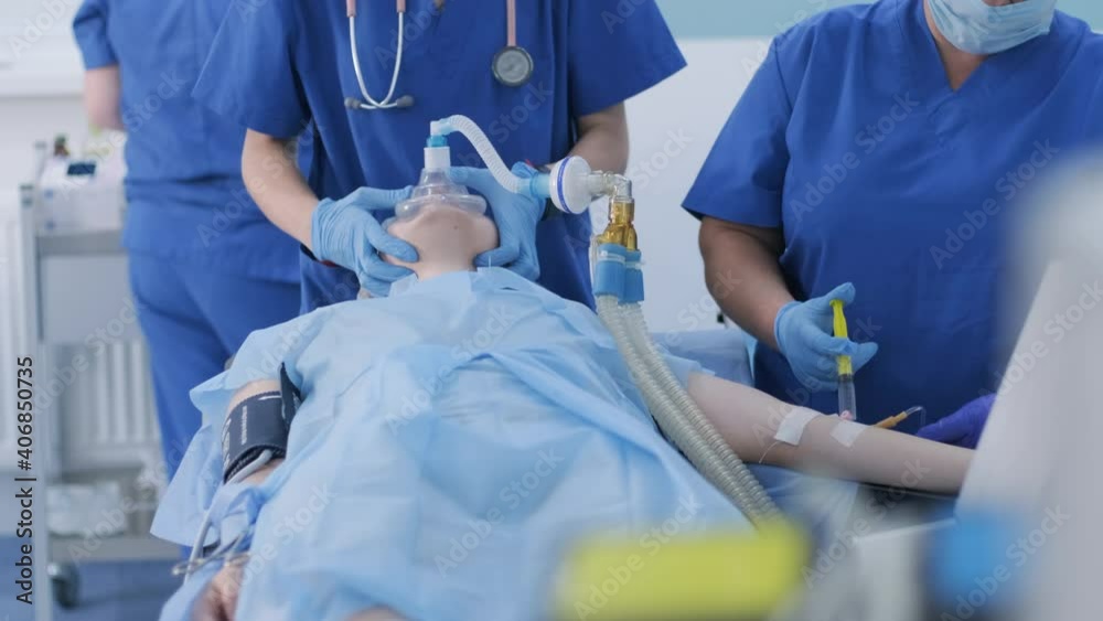 The anesthesiologist with assistant prepares female patient for surgery, puts patient into