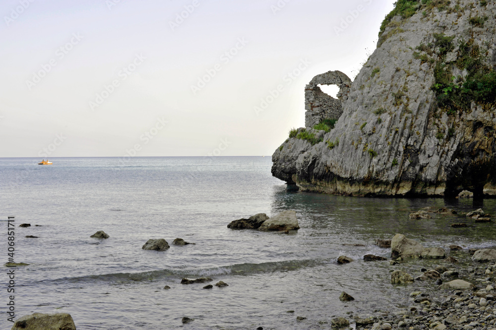 The quaint left side cliff of the inlet called Arco Naturale at sunset with the remains of an old stonework building. Palinuro, Salerno, Italy.