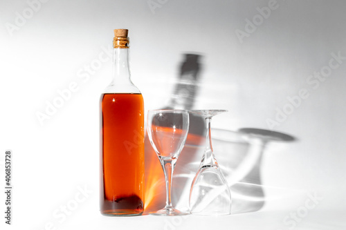 Botella con licor y copa vacia de cristal sobre fondo blanco con reflejos de flash
