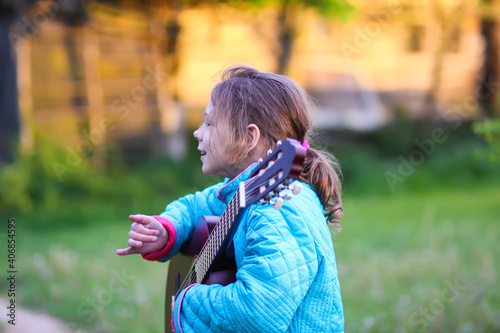 Little girl playing guitar and singing outdoors on green meadow at spring