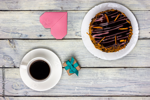 Chocolate cake, a cup of coffee, a heart shaped note and a small gift on a wooden table. Festive Flat Lay. photo