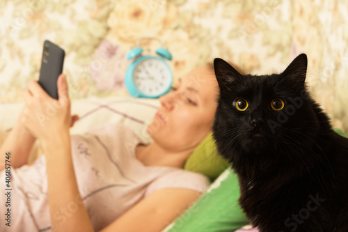 Portrait of a black cat and a woman with a phone.