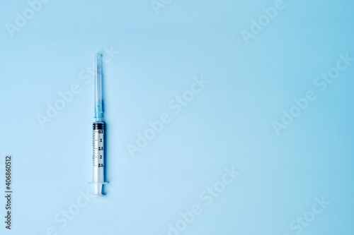 One single medical plastic disposable vaccination syringe with the needle in the cover cap isolated on the bright blue fond background