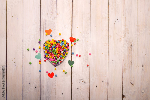 A heart-shaped box filled with rainbow-like balls on a wooden table. Colored hearts all around to remind you that love has many shades. photo