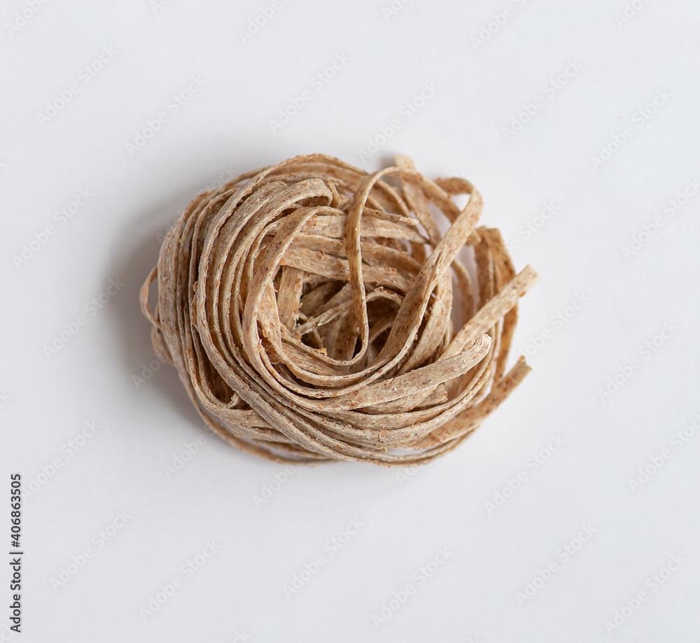 One portion raw whole grain brown pasta on a white background. Delicate wholemeal pasta made of graham flour, rich in nutrients protein, carbohydrates and fiber One portion raw whole grain brown pasta on a white background. Delicate wholemeal pasta made of graham flour, rich in nutrients protein, carbohydrates and fiber