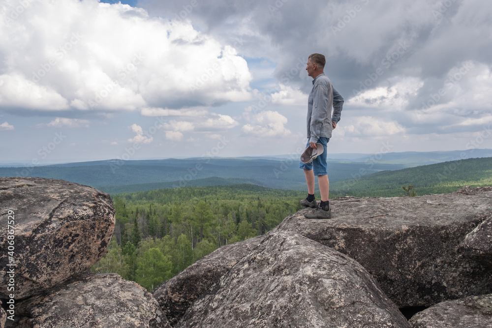 Obraz premium A middle-aged man at the top of the mountain enjoys a stunning view of the hilly valley. Freedom and goal achievement.