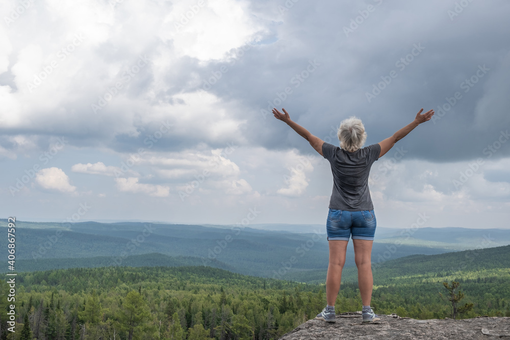 Happy middle-aged woman, raising her hands, stands on the top of the mountain. Freedom and goal achievement. Copy space. Happy middle-aged woman, raising her hands, stands on the top of the mountain. Freedom and goal achievement. Copy space.