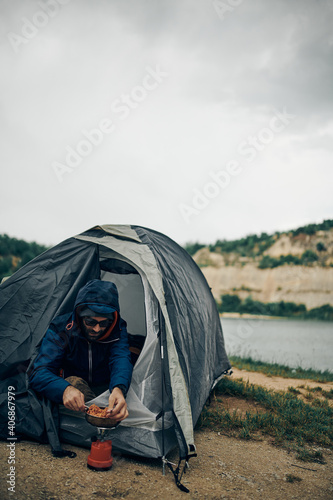 Man on a camping trip sitting in a tent and preparing lunch. Nature
