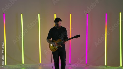 Musician playing on electric guitar against the background of multicolored neon lamps in the studio. Rock, ska punk, reggae, blues, jazz, pop music. Artist hobby is creating own melodies. Slow motion. photo
