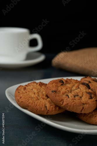 Chocolate Chip cookies with a blured cofee cup at behind and black background