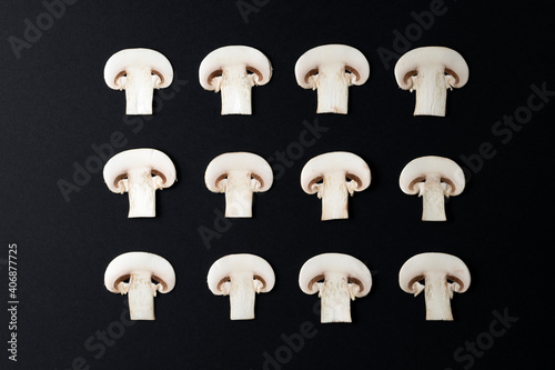 DECORATIVE PATTERN OF MUSHROOMS SLICES ORDERED AND ALIGNED ON BLACK BACKGROUND. VEGAN, VEGETARIAN AND HEALTHY LIFESTYLE CONCEPT. TOP VIEW.