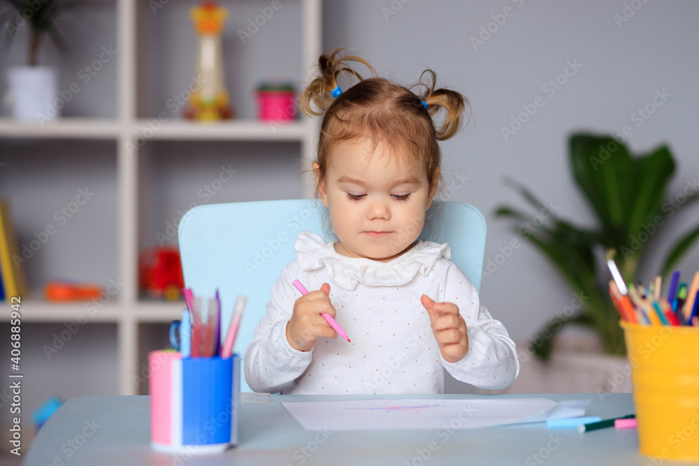 happy little girl sits at the table and draws on paper with colored pencils happy little girl sits at the table and draws on paper with colored pencils