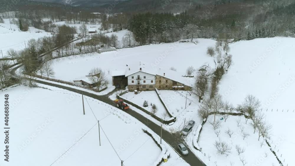 A car and snowplow drive along a clear street on a snowy winter morning. Aerial drone shot above a rural town in Spain. A car and snowplow drive along a clear street on a snowy winter morning. Aerial drone shot above a rural town in Spain.