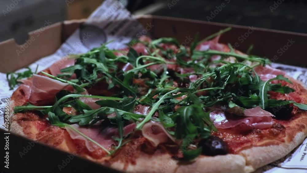 Close-up of a delicious pizza in box, while the chef adds arugula, also known as rocket, as a topping. Close-up of a delicious pizza in box, while the chef adds arugula, also known as rocket, as a topping.