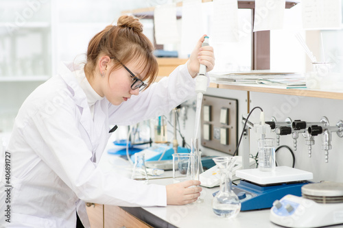 In a chemical laboratory, a girl laboratory assistant drips a solution into a measuring beaker with a special pipette