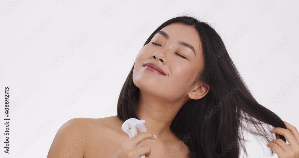 Young happy asian lady spraying her hair with conditioner, enjoying her hair care cosmetics, white studio background Young happy asian lady spraying her hair with conditioner, enjoying her hair care cosmetics, white studio background