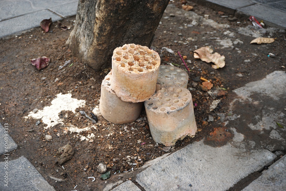 Obraz premium Burned out charcoal briquets discarded next to a tree in urban Vietnam. These pressed coal shapes are often used in street food stalls to heat pots of broth.