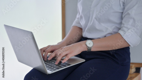 A young business woman uses a laptop placed on her leg in the office.