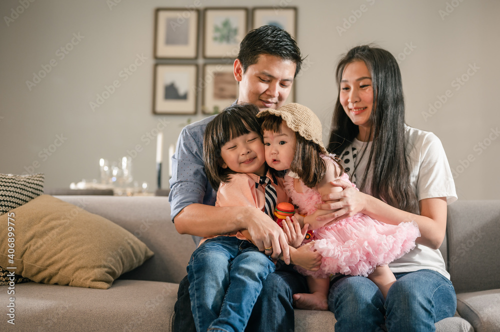 Happy family,Children sitting on the parents' lap on the sofa in the living room. The little sister in the cute hat was kissing her brother cheek.Weekend activity happy family lifestyle concept. Happy family,Children sitting on the parents' lap on the sofa in the living room. The little sister in the cute hat was kissing her brother cheek.Weekend activity happy family lifestyle concept.