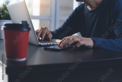 Work from home, telework concept. Man in casual wear working on laptop computer and using mobile smartphone at home office