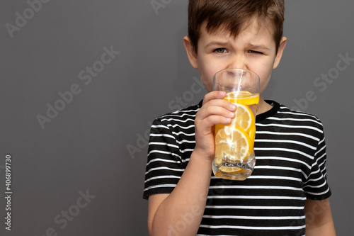 little cute boy drinks water with lemon and makes a grimace from the fact that the lemonade is sour. health concept. place to place text