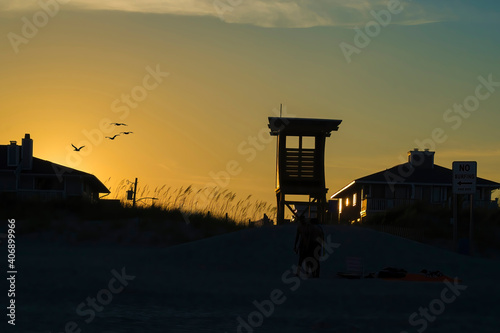 Silhouette of a lifeguard tower with seagulls flying on the yellow horizon.