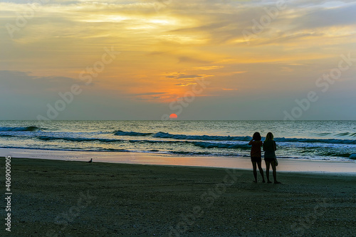 Silhouettes of couple of women gazing the orange sunrise on the horizon.