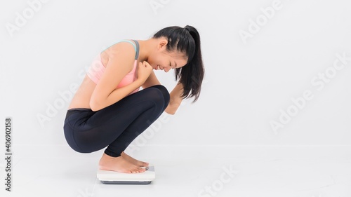 Asian happy beautiful woman resting after exercise and sitting on the weight scale at home gym background.Exercise for Lose weight,increase flexibility and tighten the shape.