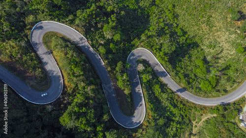 Aerial view of car driving through the forest on country road in mountain.